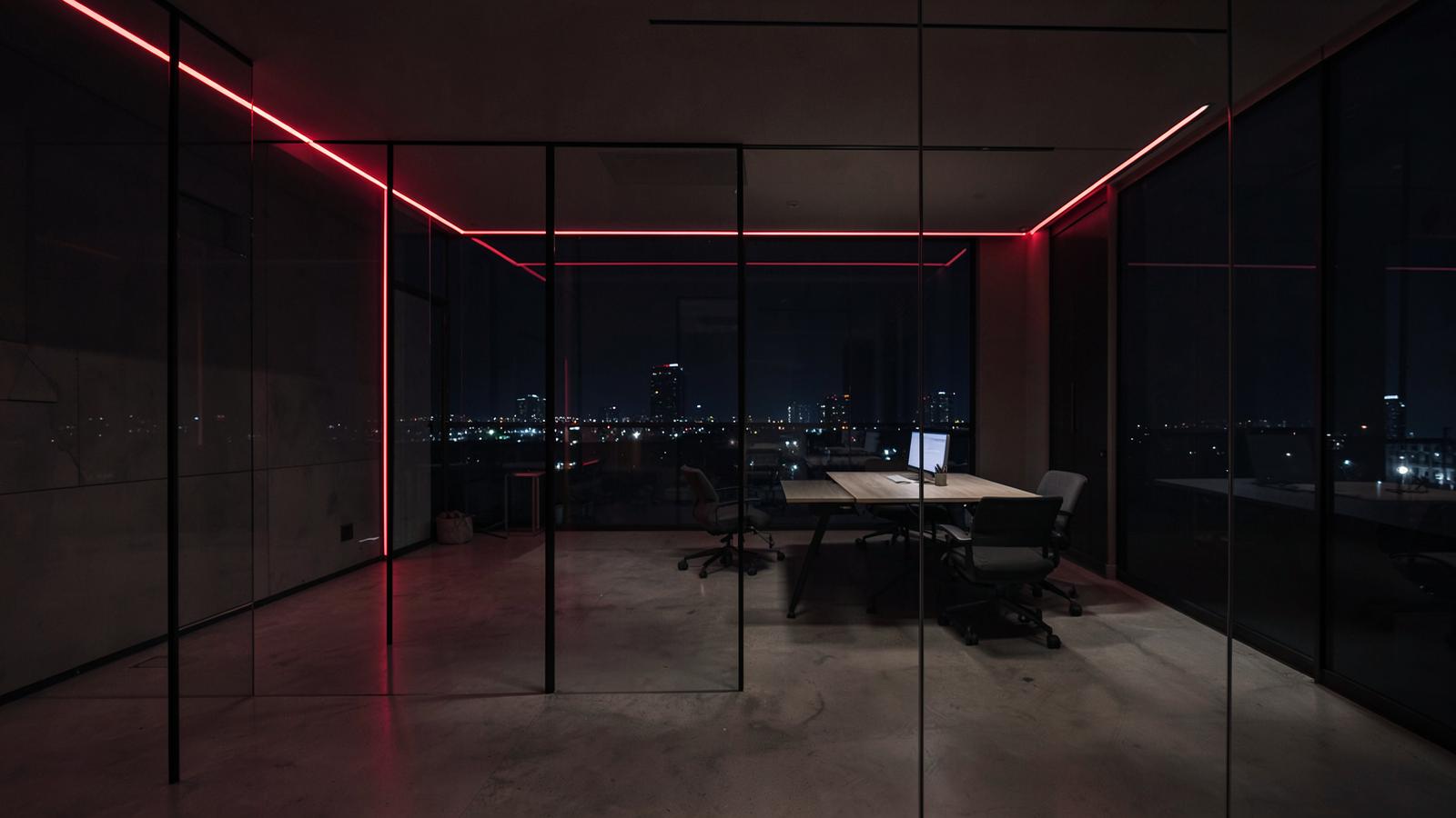 Modern glass-walled creative agency office at night with red neon accents