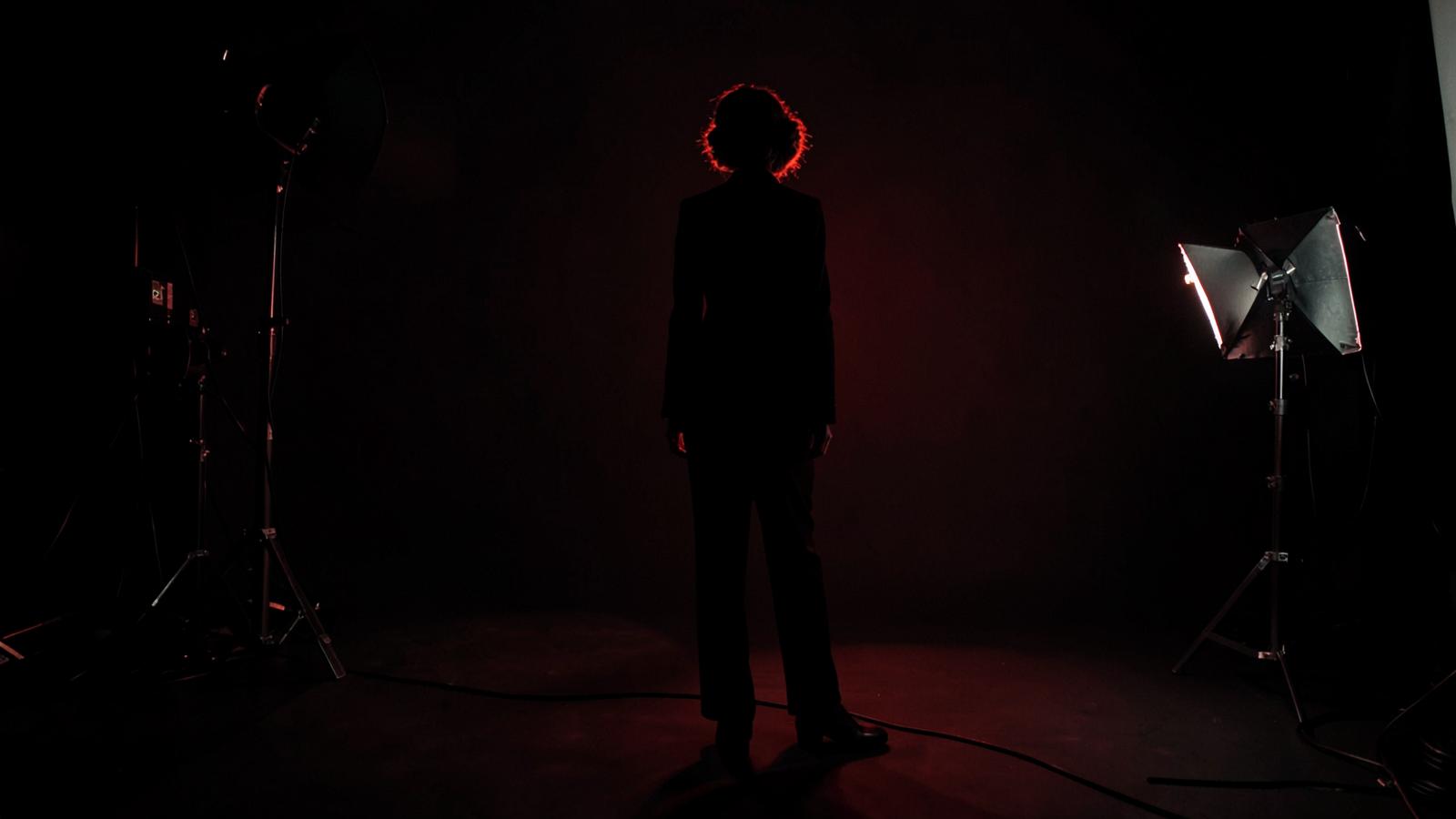Dark editorial photography studio with dramatic red rim light and model silhouette